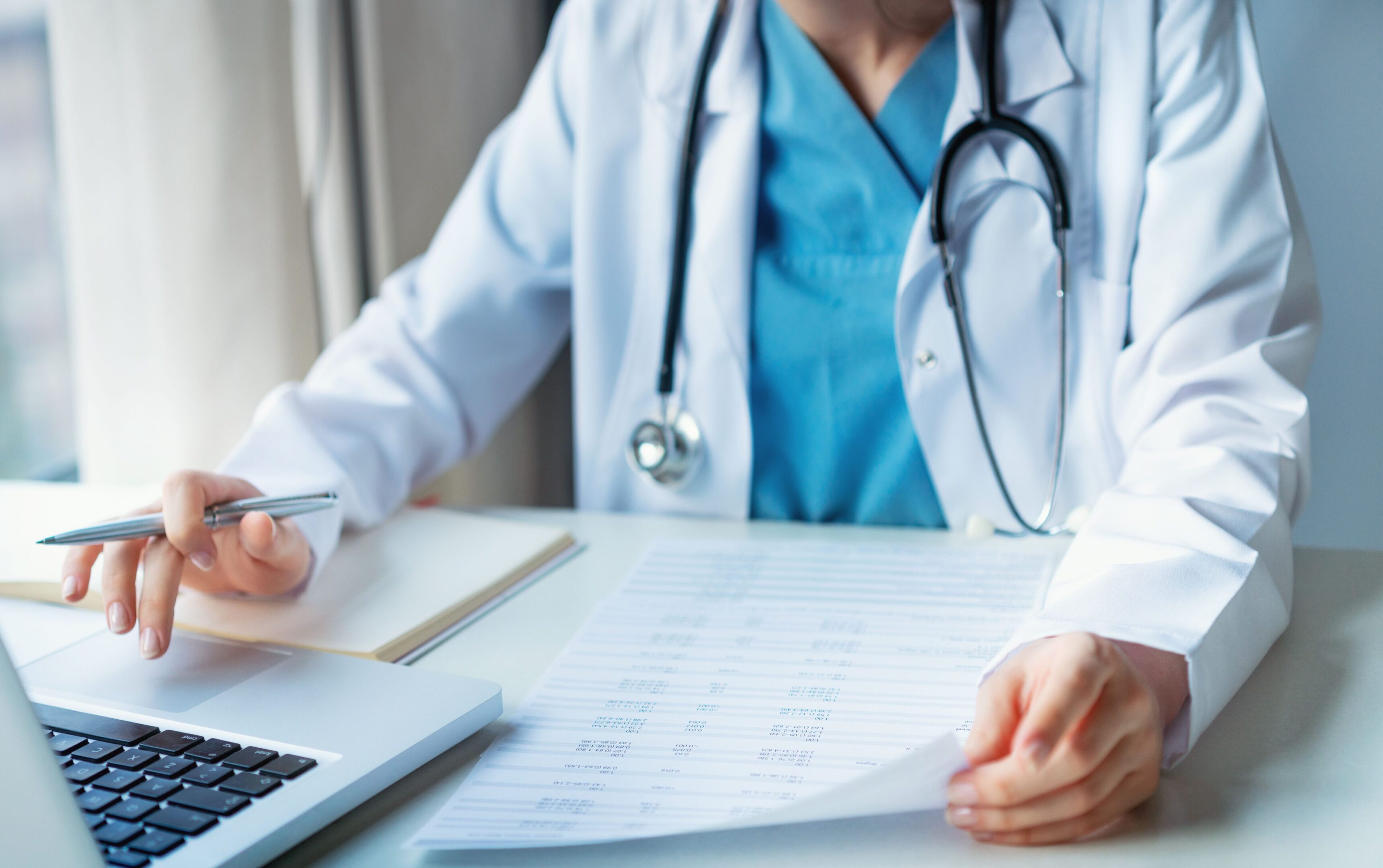 A doctor sitting at a table with papers and a laptop.