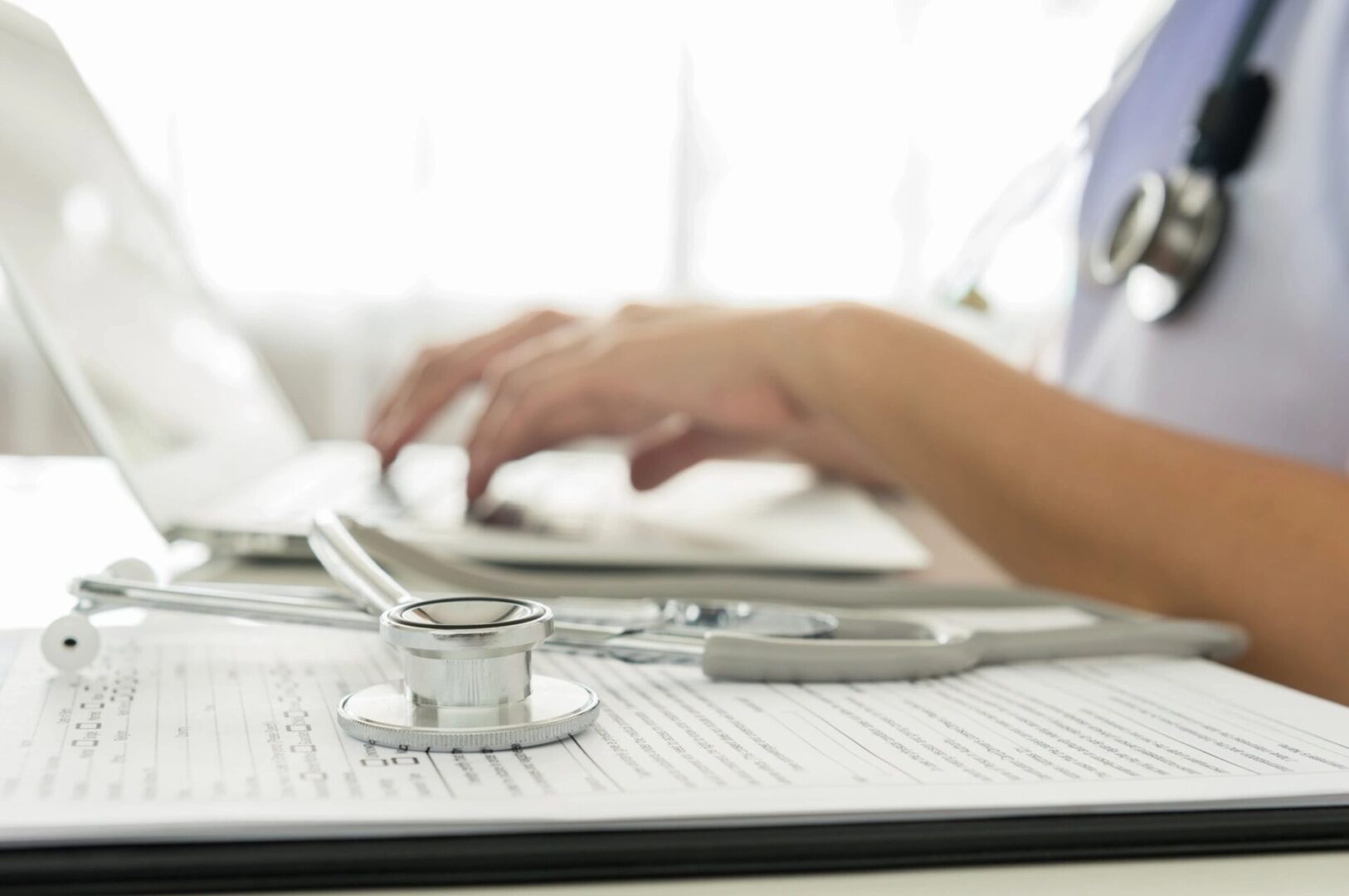 A person is typing on a laptop with a stethoscope.